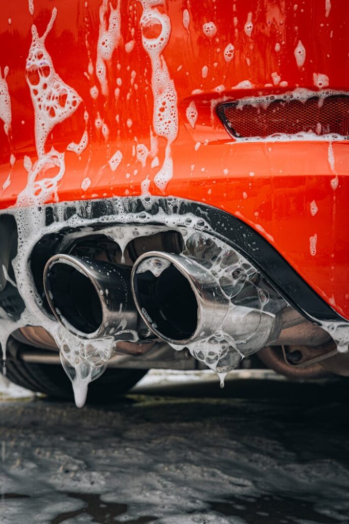 pexels photo 17356572 Detailed view of a red sports car exhaust pipe covered in foam at a car wash.